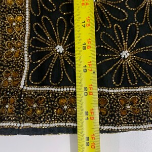 May include: Black fabric with gold and white beading in a floral pattern. A yellow measuring tape is to the right of the fabric, showing a measurement of 23 inches.