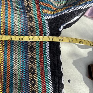Pode incluir: Um colorido moletom Baja tecido com um padr&atilde;o listrado em tons de azul, laranja, verde e preto. O moletom com capuz &eacute; medido com uma fita m&eacute;trica amarela, mostrando um comprimento de aproximadamente 58 cm.