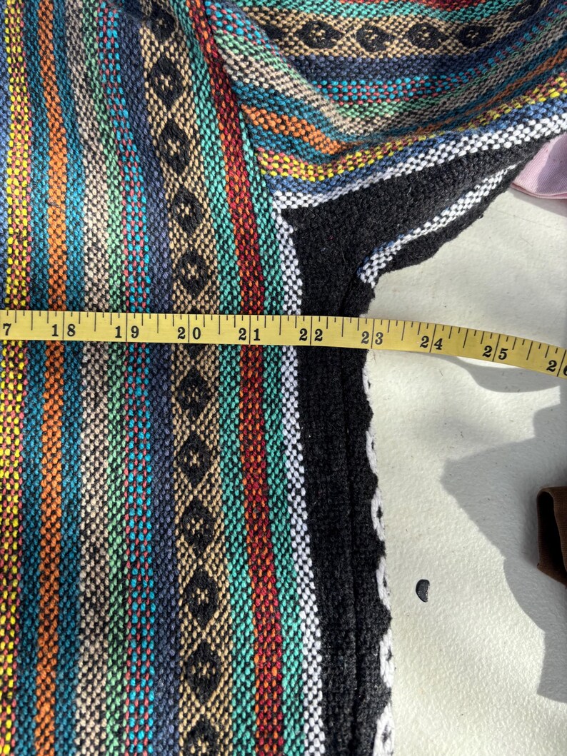 Pode incluir: Um colorido moletom Baja tecido com um padr&atilde;o listrado em tons de azul, laranja, verde e preto. O moletom com capuz &eacute; medido com uma fita m&eacute;trica amarela, mostrando um comprimento de aproximadamente 58 cm.