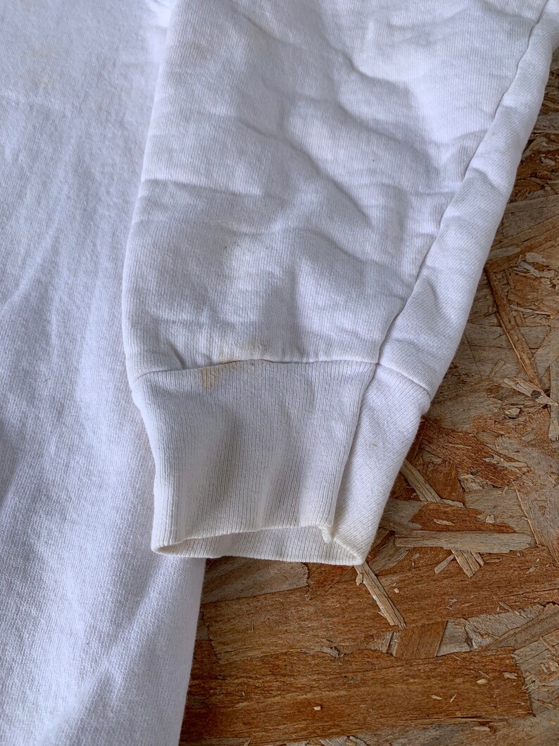 May include: White long-sleeved sweatshirt with a ribbed cuff. The sweatshirt is made of a soft, comfortable fabric.