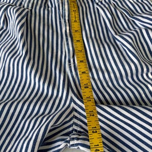 Puede incluir: Primer plano de unos pantalones cortos a rayas azules y blancas con una cinta m&eacute;trica amarilla. La cinta muestra una medida de aproximadamente 38 cm. Los pantalones cortos tienen un patr&oacute;n de rayas verticales y una cremallera.
