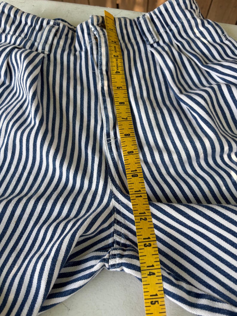 Puede incluir: Primer plano de unos pantalones cortos a rayas azules y blancas con una cinta m&eacute;trica amarilla. La cinta muestra una medida de aproximadamente 38 cm. Los pantalones cortos tienen un patr&oacute;n de rayas verticales y una cremallera.