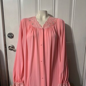 May include: A pink, long-sleeved nightgown with a lace trim around the neckline and cuffs. The gown has a button-up front and is made of a soft, silky fabric.