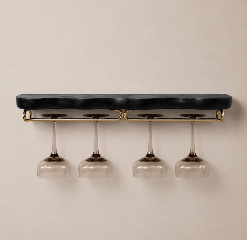 May include: A wall-mounted shelf featuring a thick, black, textured wooden top with an irregular edge. Attached to the underside is a gold-toned metal rack designed to hold four stemmed wine glasses, which are hanging upside down by their bases.
