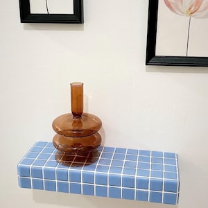 Puede incluir: Una estanter&iacute;a de azulejos azules con un jarr&oacute;n de vidrio marr&oacute;n en la parte superior. El jarr&oacute;n tiene una forma redonda y bulbosa y est&aacute; hecho de tres piezas apiladas.