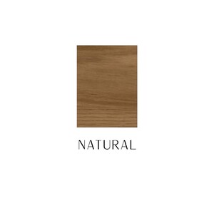 May include: A rectangular swatch of light brown wood grain with a smooth finish. Below the wood sample, the word NATURAL is printed in a simple, thin, black sans-serif font. The wood features visible horizontal grain patterns and light brown tones.