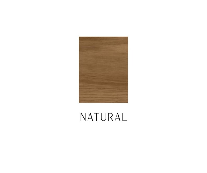 May include: A rectangular swatch of light brown wood grain with a smooth finish. Below the wood sample, the word NATURAL is printed in a simple, thin, black sans-serif font. The wood features visible horizontal grain patterns and light brown tones.
