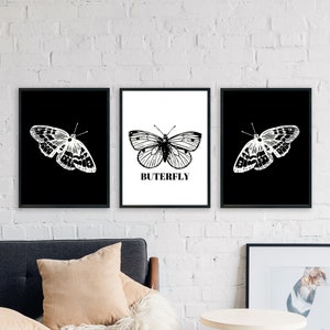 May include: Three black framed prints with white butterflies on a white brick wall. The center print has the word "BUTERFLY" printed below the butterfly.