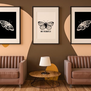 May include: Three framed black and white butterfly illustrations with the word "BUTTERFLY" printed below the center image. Two brown leather armchairs and a wooden coffee table with a black lamp on top are in front of the wall.