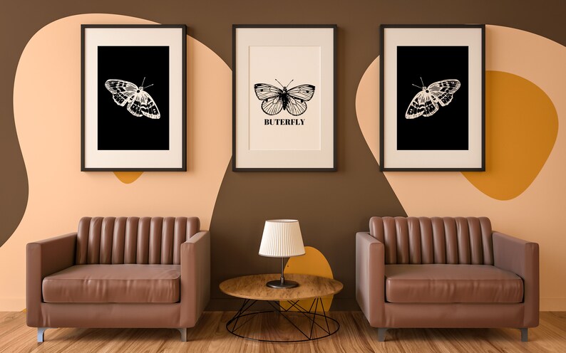 May include: Three framed black and white butterfly illustrations with the word "BUTTERFLY" printed below the center image. Two brown leather armchairs and a wooden coffee table with a black lamp on top are in front of the wall.