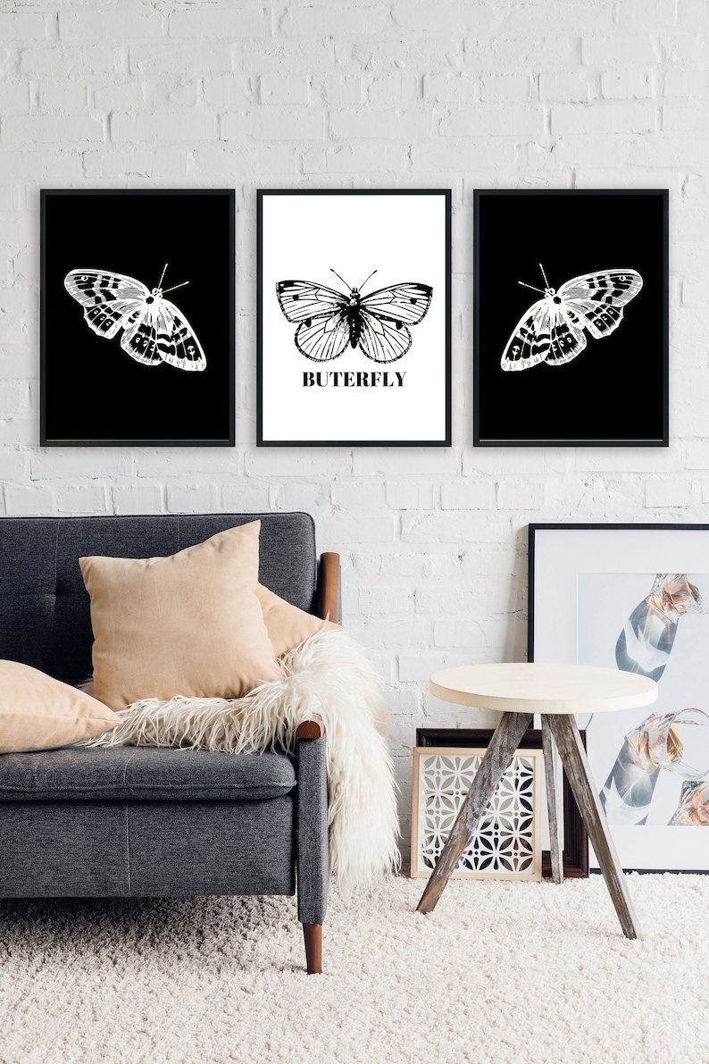 May include: Three black framed prints with white butterflies on a white brick wall. The center print has the word "BUTERFLY" printed below the butterfly.