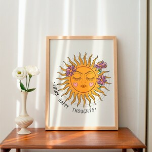 Puede incluir: Una impresi&oacute;n enmarcada con un sol amarillo con una cara y los ojos cerrados. El sol est&aacute; rodeado de flores rosas y el texto "Think Happy Thoughts." est&aacute; escrito debajo del sol.
