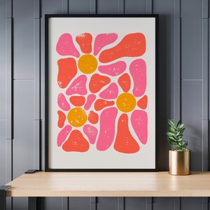 May include: A framed print with a retro abstract design featuring pink and orange shapes resembling flowers. The print has a white background and a black frame.