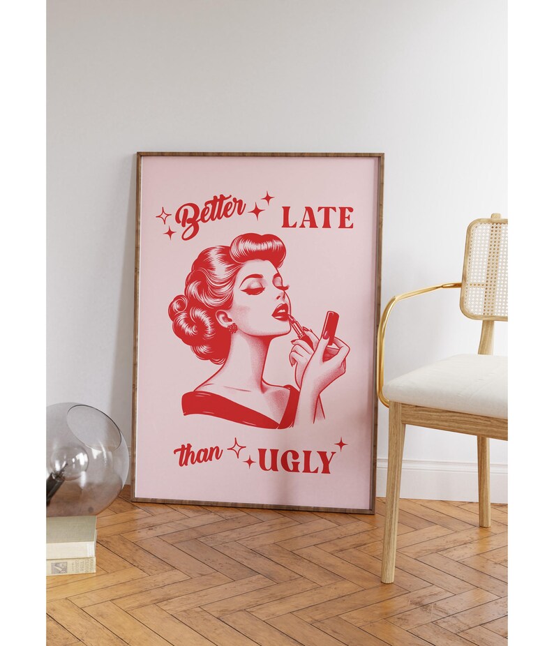 Pu&ograve; includere: Una stampa incorniciata rosa con un'illustrazione rossa di una donna che si applica il rossetto. Il testo sulla stampa recita "Better Late than Ugly."