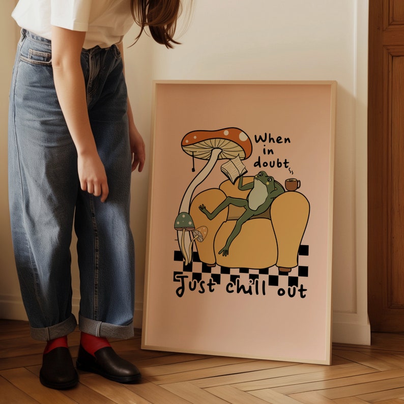 May include: A pink framed poster with a cartoon frog sitting in a yellow armchair. The frog is reading a book and holding a cup of coffee. The poster has the text "When in doubt, just chill out" and a mushroom with a red cap.