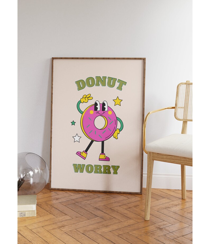 May include: A framed print with a pink donut character with green eyes and a yellow smile. The donut is wearing green shoes and has a green peace sign on its hand. The text "DONUT WORRY" is written in green letters on a beige background.