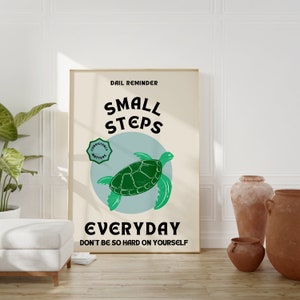 Pu&ograve; includere: Un poster beige con un'illustrazione di una tartaruga marina verde e il testo "Daily Reminder Small Steps Everyday Don't be so hard on yourself".