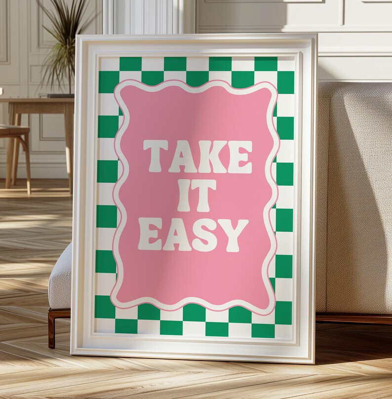 May include: A white framed print with a pink background and green and white checkered border. The text "TAKE IT EASY" is written in white on the pink background.