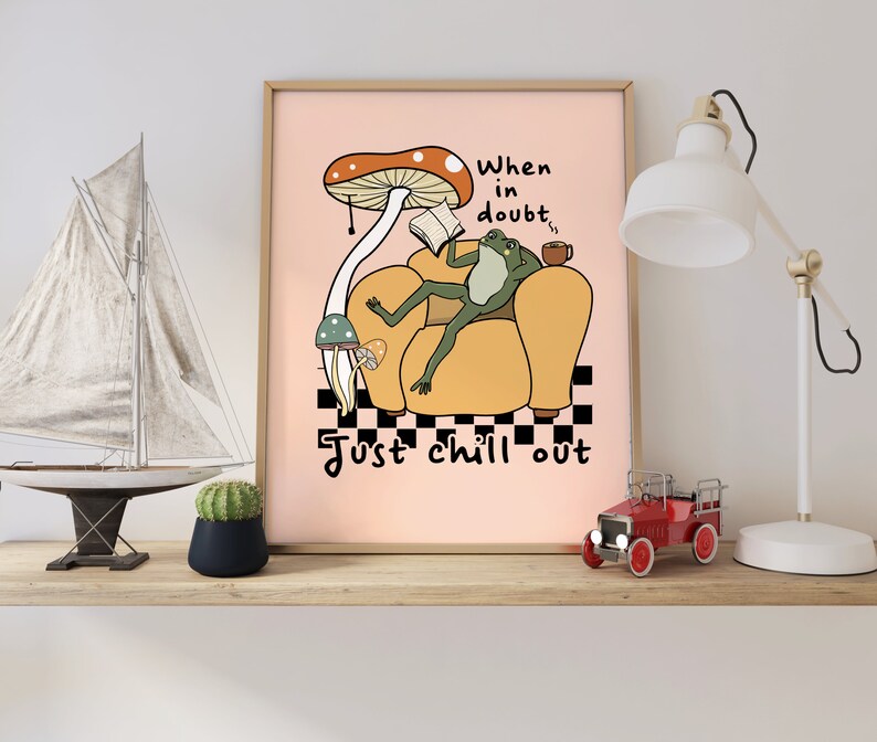 May include: A pink poster with a cartoon frog sitting in a yellow armchair, reading a book and holding a cup. The frog is under a large red and white mushroom. The text on the poster reads "When in doubt, just chill out".