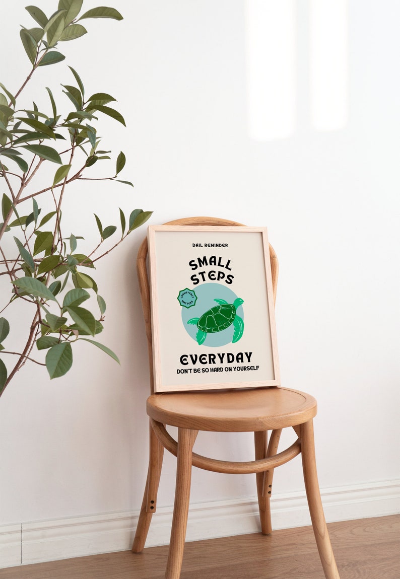 Pu&ograve; includere: Un poster motivazionale incorniciato con uno sfondo blu chiaro e un'illustrazione di una tartaruga verde. Il testo recita "Promemoria quotidiano: Piccoli passi ogni giorno. Non essere troppo duro con te stesso."