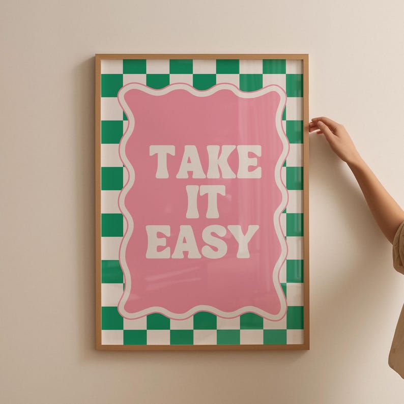 May include: A framed print with a green and white checkered background. The print features a pink, wavy-edged sign with the text "TAKE IT EASY" in white letters.