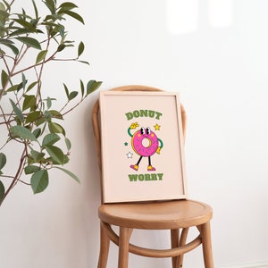 May include: A framed print with a pink donut character with green eyes and a green smile. The donut is wearing shoes and has a green star above its head. The text "DONUT WORRY" is written in green letters below the donut.