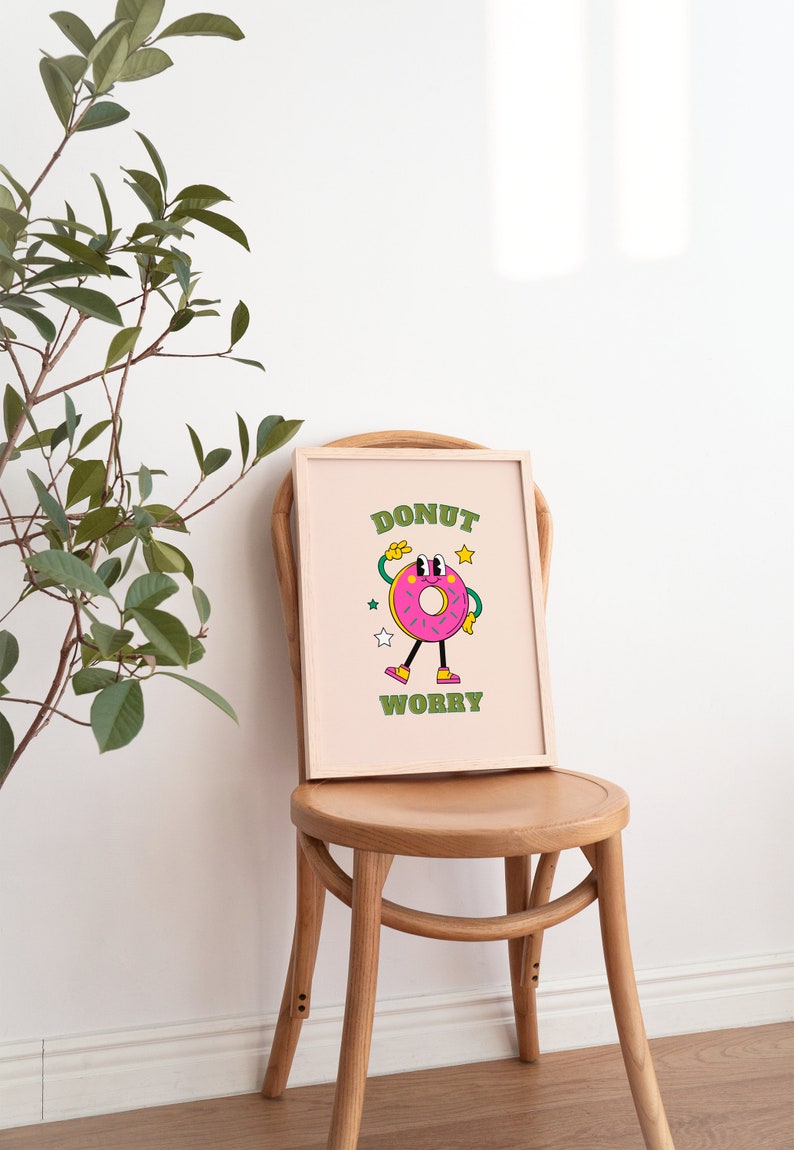 May include: A framed print with a pink donut character with green eyes and a green smile. The donut is wearing shoes and has a green star above its head. The text "DONUT WORRY" is written in green letters below the donut.