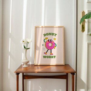 May include: A framed print with a pink donut character with green eyes and arms. The donut is wearing green shoes and has a pink and white sprinkle design. The text "Donut Worry" is written in green letters below the donut.