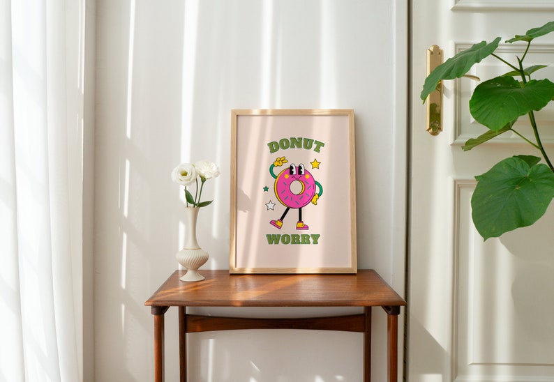 May include: A framed print with a pink donut character with green eyes and arms. The donut is wearing green shoes and has a pink and white sprinkle design. The text "Donut Worry" is written in green letters below the donut.