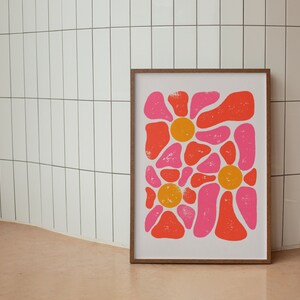 May include: A framed print of an abstract floral design with pink and orange shapes. The print is on a white background and has a distressed look.