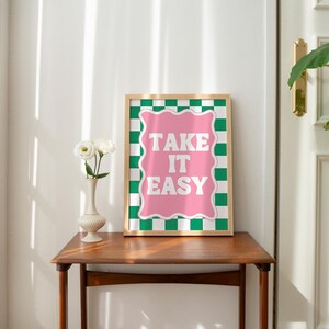 May include: A framed print with a pink and green checkered background. The print features the text "TAKE IT EASY" in white letters.