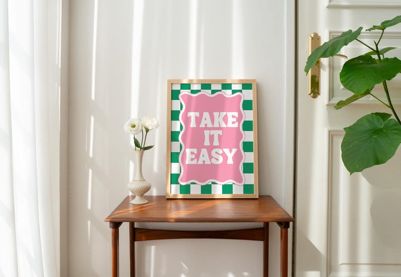 May include: A framed print with a pink and green checkered background. The print features the text "TAKE IT EASY" in white letters.