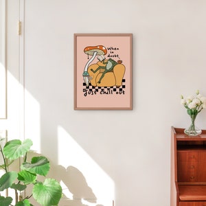 May include: A pink framed print with a cartoon frog sitting in a yellow armchair with a mushroom above its head. The text reads "When in doubt, just chill out".