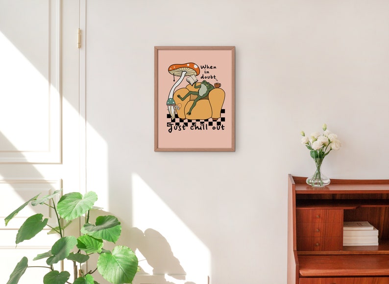 May include: A pink framed print with a cartoon frog sitting in a yellow armchair with a mushroom above its head. The text reads "When in doubt, just chill out".