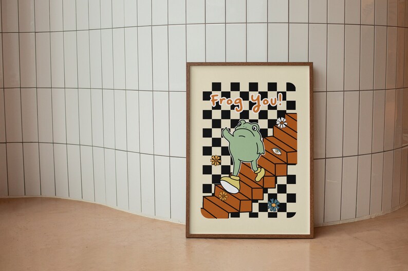 May include: A framed print featuring a green frog ascending a set of stairs against a checkered backdrop. The print reads "Frog You!" in black text.