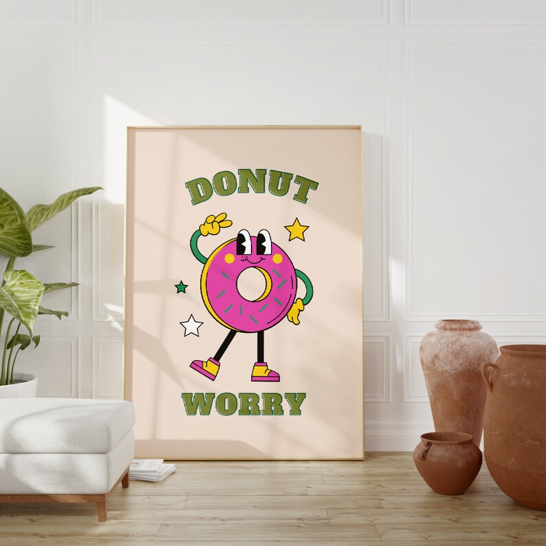 May include: A pink donut with green sprinkles and a smiling face is depicted on a beige poster with the text "DONUT WORRY" in green letters. The poster is framed in a light brown frame and is hanging on a white wall.