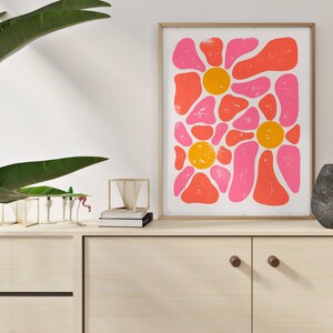May include: Abstract art print with pink and orange shapes in a floral pattern. The print is framed in a light wood frame and is hanging on a white wall.