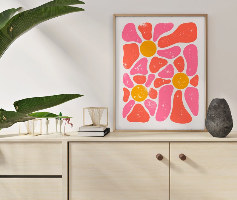 May include: Abstract art print with pink and orange shapes in a floral pattern. The print is framed in a light wood frame and is hanging on a white wall.