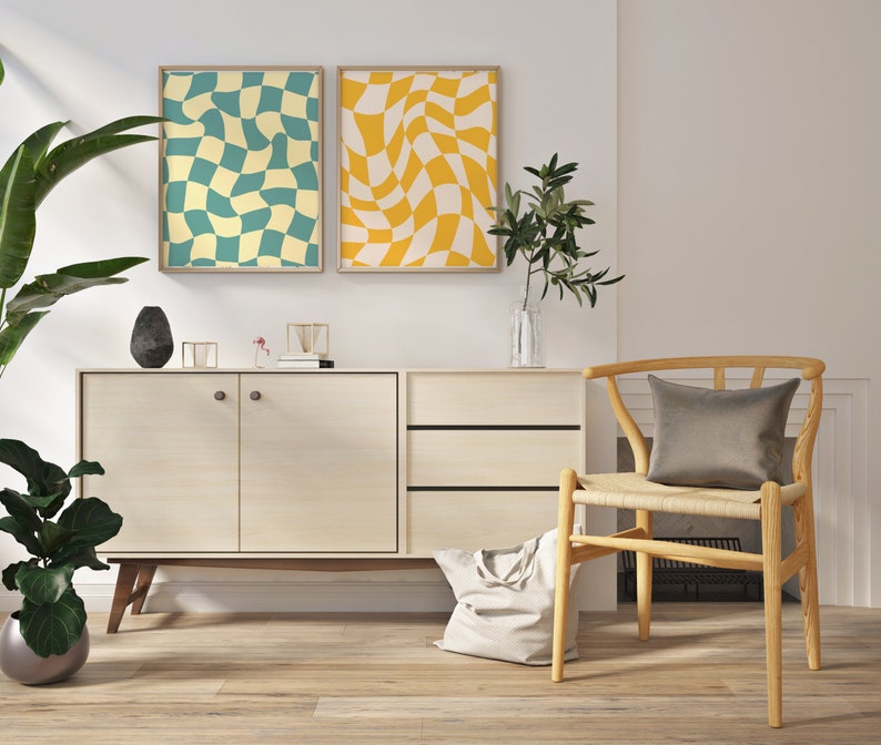 May include: Two abstract geometric prints in yellow and blue hang above a light wood cabinet with two doors and two drawers. A woven chair with a gray cushion sits to the right of the cabinet.