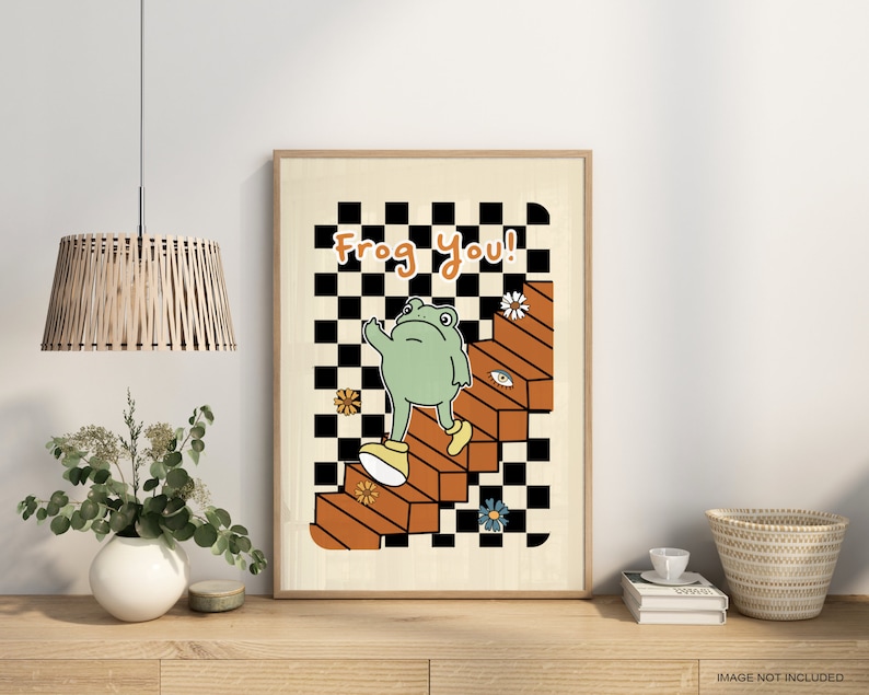 May include: A framed print featuring a green frog ascending a set of stairs against a checkered backdrop. The text "Frog You!" is displayed at the top of the print.