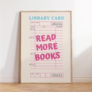 May include: A framed print featuring a vintage library card design. The text "LIBRARY CARD" is in blue, with the words "READ MORE BOOKS" in pink. The print has a beige background and a wooden frame, suitable for a home library or reading nook.