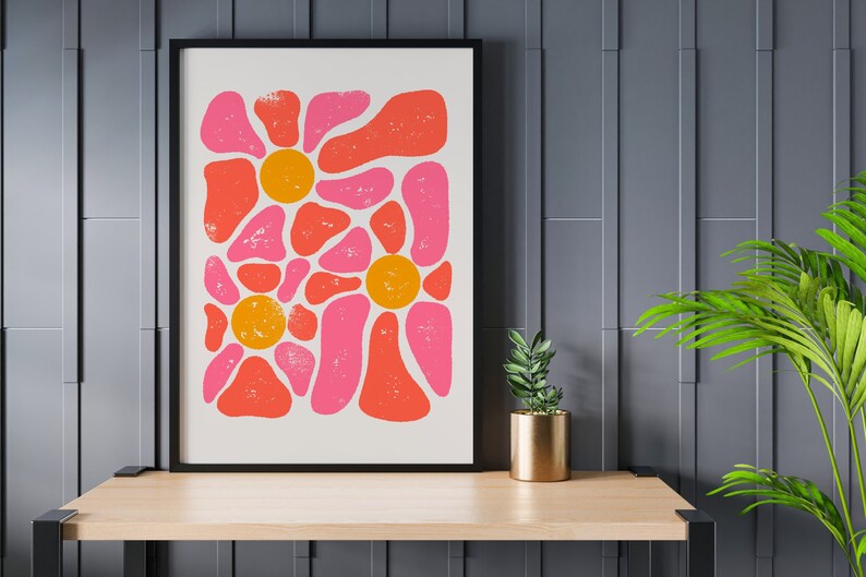 May include: A framed print with a retro abstract design featuring pink and orange shapes resembling flowers. The print has a white background and a black frame.