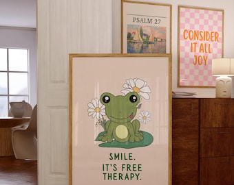 May include: A framed art print featuring a cartoon frog with daisies, sitting on a lily pad. The print has the text "SMILE. IT'S FREE THERAPY." Two other framed prints are visible, one with the text "CONSIDER IT ALL JOY" and another with the text "PSALM 27".