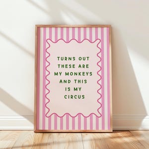 May include: A framed art print with a pink and white striped background. The print features a pink scalloped border around a light pink centre with the text "TURNS OUT THESE ARE MY MONKEYS AND THIS IS MY CIRCUS" in green lettering.