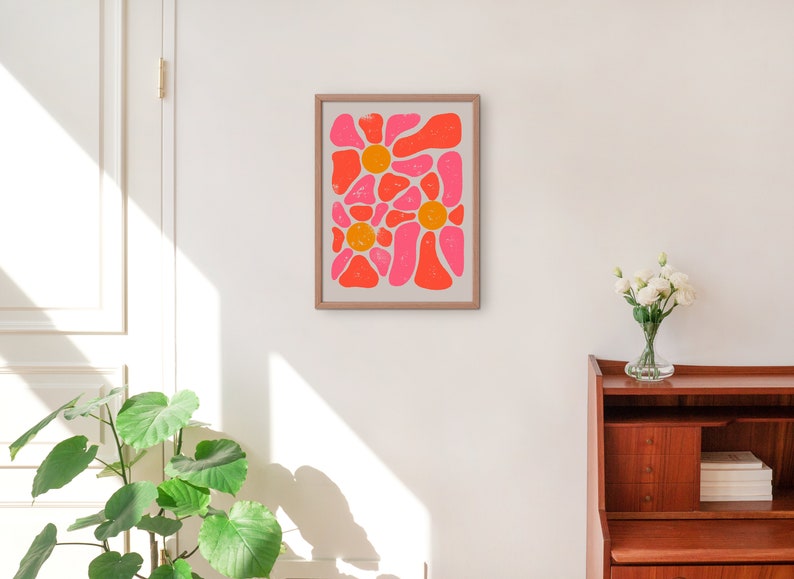 May include: A framed abstract print with a pink and orange floral design. The print is in a light wood frame and is hanging on a white wall.
