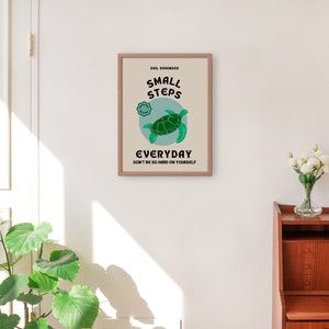 Pu&ograve; includere: Un poster motivazionale incorniciato con sfondo blu chiaro e una tartaruga marina verde. Il poster recita "Small Steps Everyday Don't be so hard on yourself".