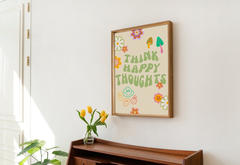 May include: A framed print with a light beige background and green text that reads "Think Happy Thoughts". The text is surrounded by colorful flowers, smiley faces, and mushrooms.
