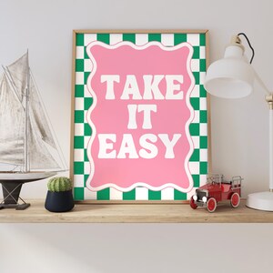 May include: A framed print with a green and white checkered background and a pink speech bubble with the text "TAKE IT EASY" in white letters.
