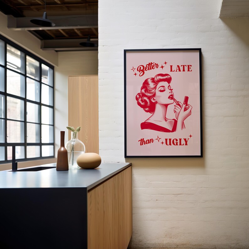Pu&ograve; includere: Un poster rosso e bianco con un'illustrazione vintage di una donna che si applica il rossetto. Il testo sul poster recita "Better Late than Ugly".