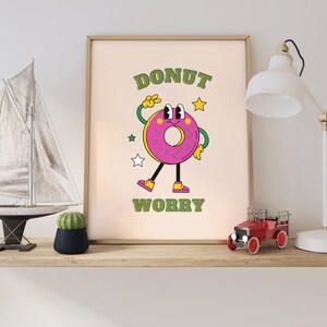 May include: A framed print with a cartoon donut character with the text "DONUT WORRY" in green letters. The donut is pink with green sprinkles and a smiling face. The background is a light beige color.